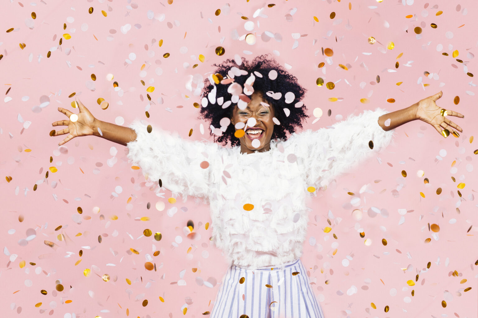 Happy young woman celebrating with arms out and lots of falling confetti